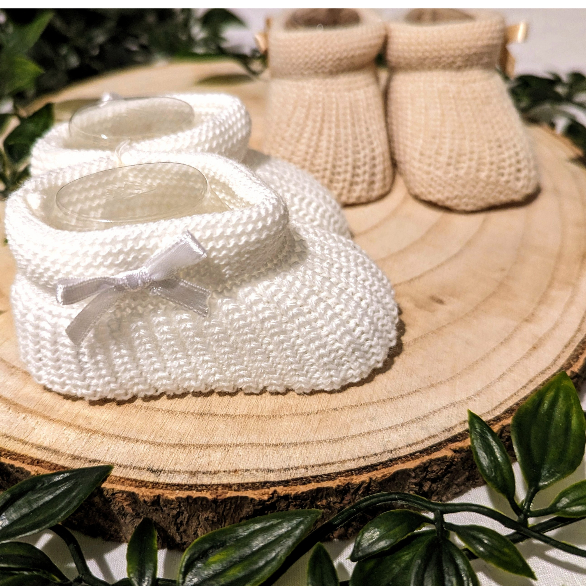 Unisex Newborn Clothes - Baby booties with a white coloured knitted design, featuring a small bow on the side. (Featured on a neutral background)