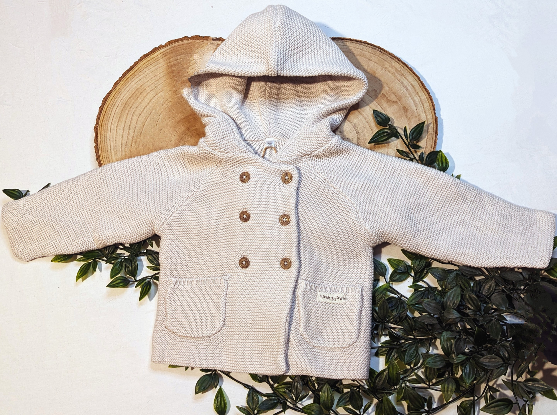 Baby cardigan, knitted in beige organic cotton. Features an adorable hood, double breasted wooden button fastenings and two pockets for practicality.