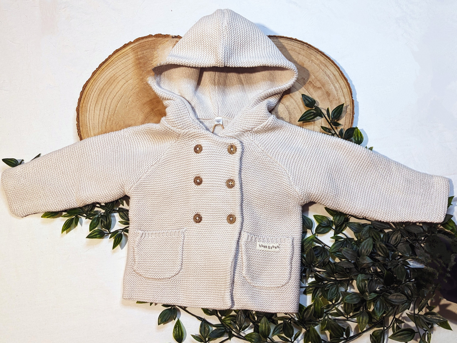 Unisex baby cardigan made from organic cotton. Beige colour with double breast wooden button. Knitted design with hood and 2 pockets. 